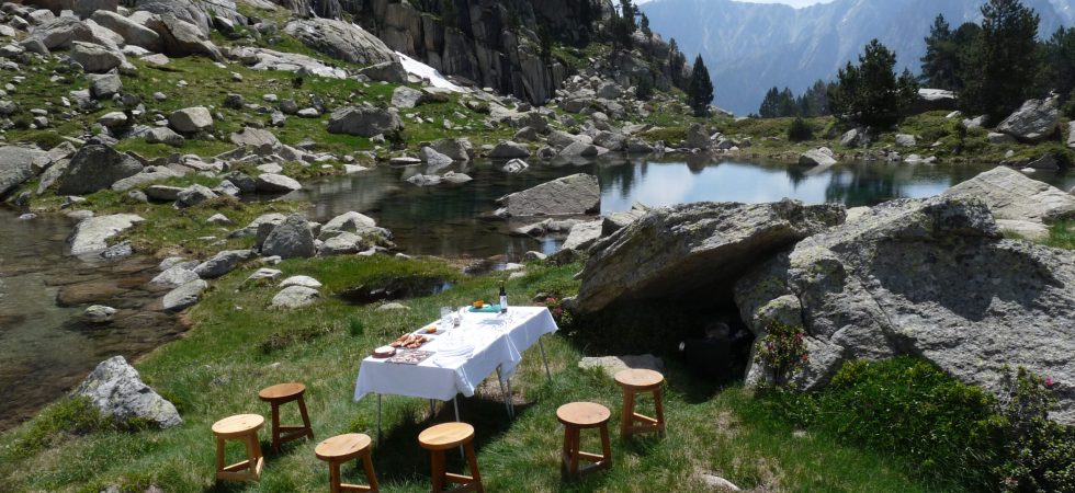 Picnic exclusivo en el Parque Nacional de los Pirineos: mesa y tamburetes frente a un lago rodeado de naturaleza.