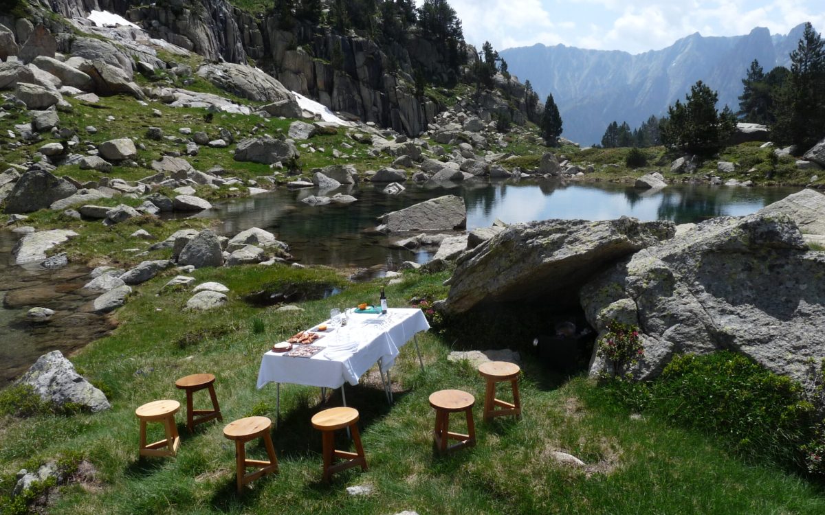 Exclusive Picnic in the Pyrenees National Park: table and stools by a lake surrounded by nature.